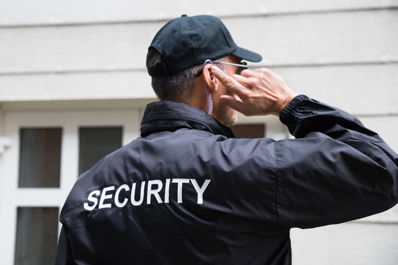 Rear view of mature security guard listening to earpiece against building